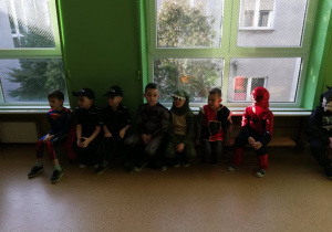 Chłopcy w strojach przebierańców siedzą na ławeczce w sali gimnastycznej.