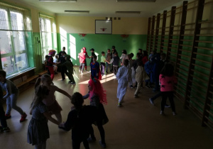 Dzieci tańczą na sali gimnastycznej do muzyki karnawałowej.