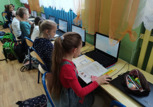 Kilkoro dzieci siedzi przy laptopach w pracowni komputerowej.