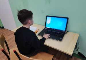 Chłopiec siedzi przy laptopach w pracowni komputerowej.