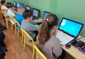 Kilkoro dzieci siedzi przy laptopach w pracowni komputerowej.