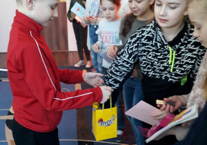 Chłopiec częstuje dziewczynki słodkim batonikiem.