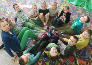 11 dzieci wraz z wychowawczynią siedzi w kole, prezentując swoje kolorowe skarpetki.