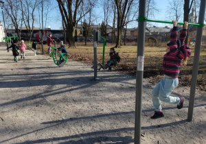 Dzieci ćwiczą na przyrządach obok placu zabaw w parku.