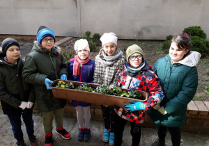 Grupa uczniów pokazuje swój mały ogródek.