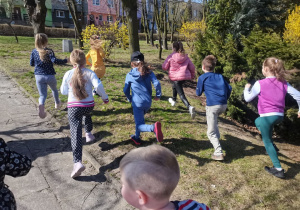 Dzieci biegną w szkolnym ogrodzie, szukają upominków od wielkanocnego zajączka.
