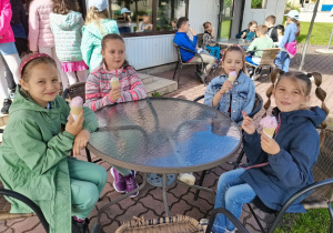 4 dziewczynki siedzą przy stoliku i jedzą lody.