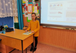 Uczennica stoi przy biurku nauczyciela.