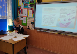Uczeń siedzi za biurkiem nauczyciela.