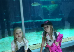 2 dziewczynki pozują na tle akwarium.