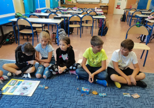 Uczniowie siedzą na dywanie, opowiadają o wakacjach i prezentują pamiątki.