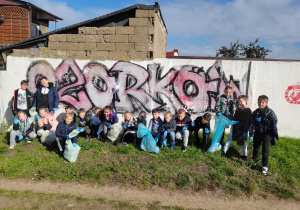 Dzieci pozują do zdjęcia z wypełnionymi workami śmieci na tle napisu "Ozorków".