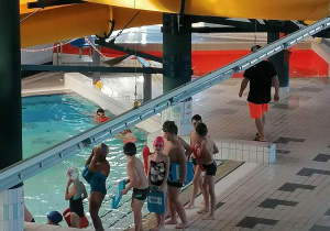 Dzieci trenują pływanie na małym basenie.