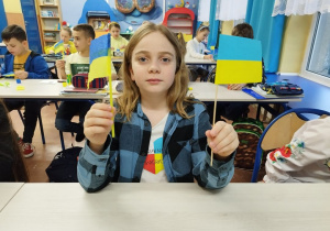 Uczeń prezentuje wykonane własnoręcznie chorągiewki ukraińskie.