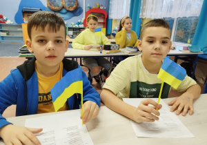 Uczniowie prezentują wykonane własnoręcznie chorągiewki ukraińskie.