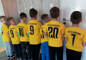 Chłopcy prezentują koszulki z logo szkoły i swoimi numerami