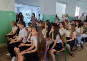 Uczniowie słuchają siedząc w holu szkoły
