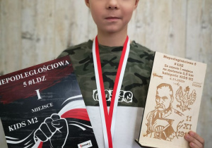 Rafał prezentuje zdobyty medal, dyplom i statuetkę.
