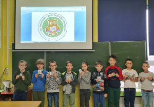 Uczniowie klasy IIIc stoja pod tablicą z odznakami z okazji Dnia Tabliczki Mnożenia.