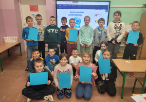 Uczniowie z kartkami w symbolicznym kolorze niebieskim
