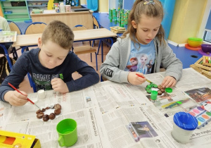 Dzieci malują świeczniki z kasztanów.