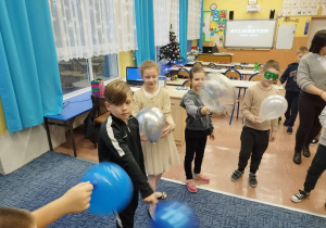 Dzieci tańczą z balonikami w kole na dywanie
