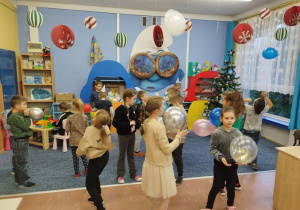 Dzieci tańczą z balonikami na dywanie w klasie
