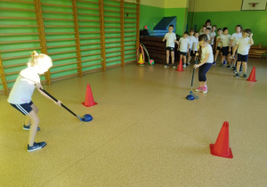 Uczniowie uczą sie prawidłowo trzymać i wykorzystywać kij do hokeja.