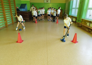 Uczniowie uczą sie prawidłowo trzymać i wykorzystywać kij do hokeja.