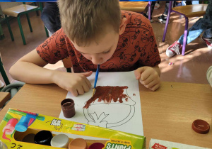 Dziecko maluje pędzelkiem za pomocą ust.