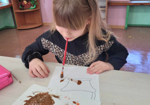 Dziecko maluje pędzelkiem za pomocą ust.