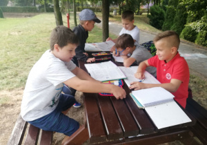 Pięciu chłopców odrabia lekcje przy stoliczku na szkolnym podwórku