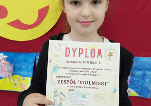 Uczennica kl. 1a pozuje w klasie z dyplomem.